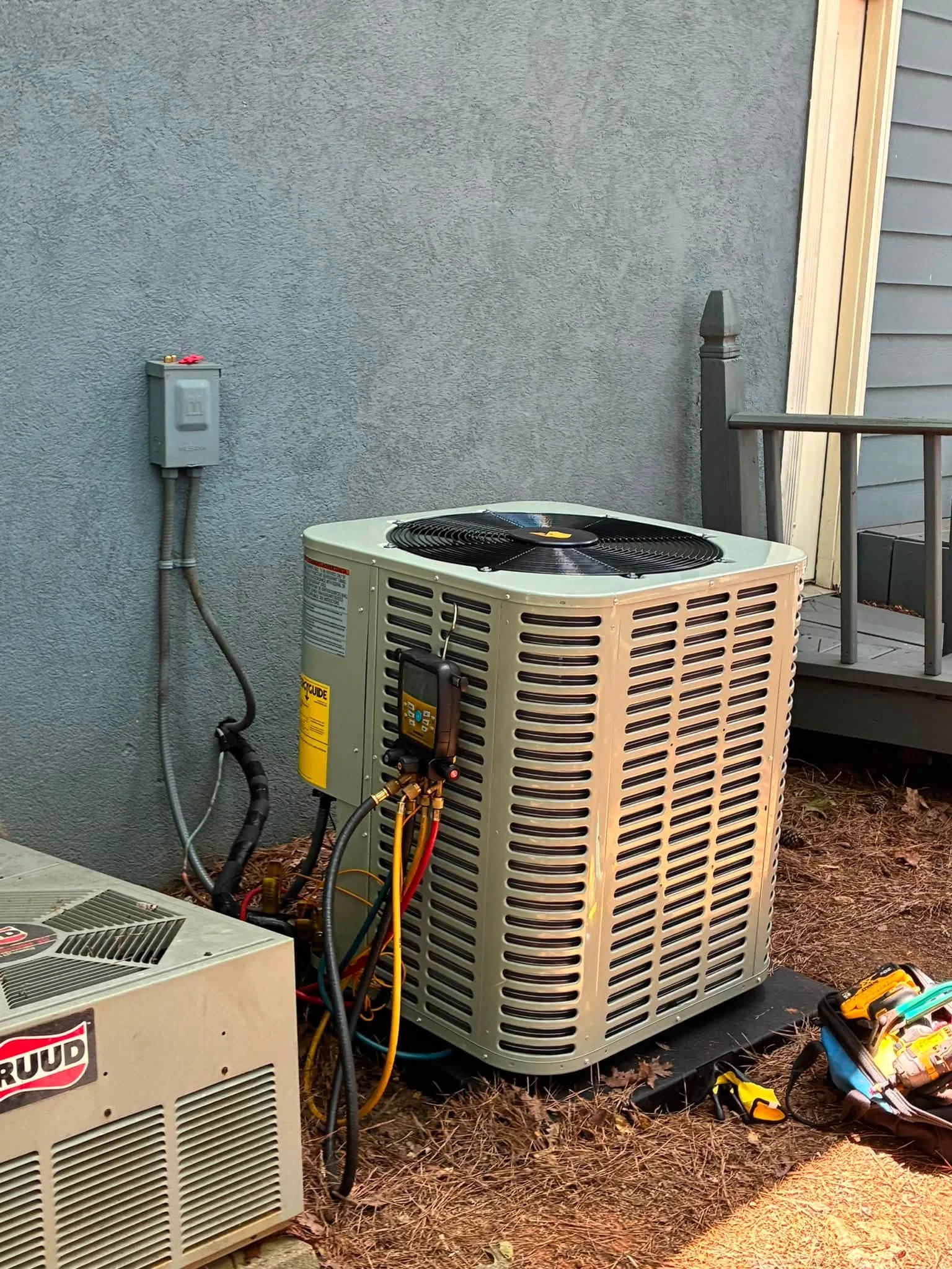 Installed AC condenser unit with fan, electrical disconnect, and refrigerant lines on concrete pad