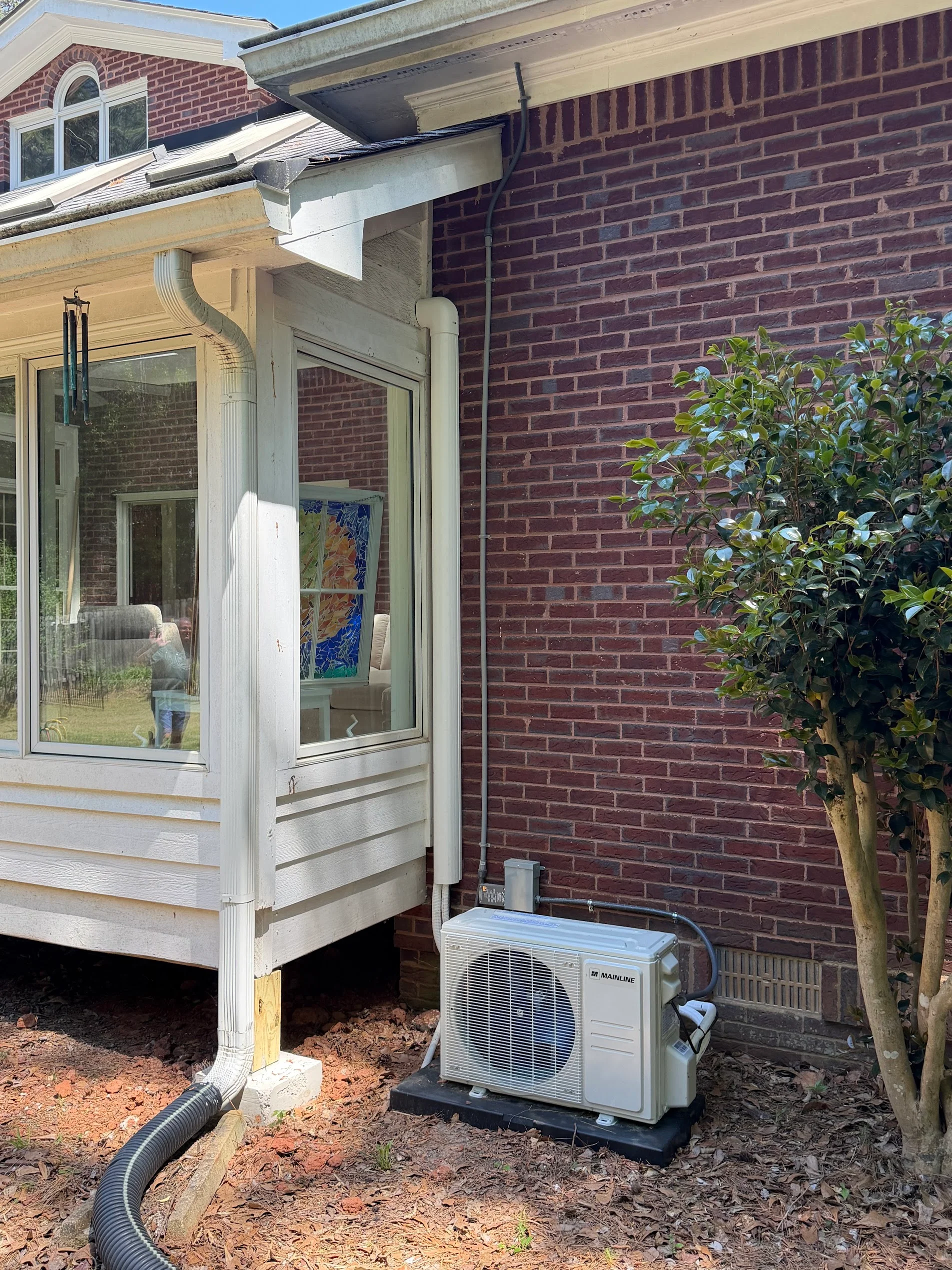 Ductless mini-split outdoor compressor unit installed beside brick home with refrigerant lines and condensate drain