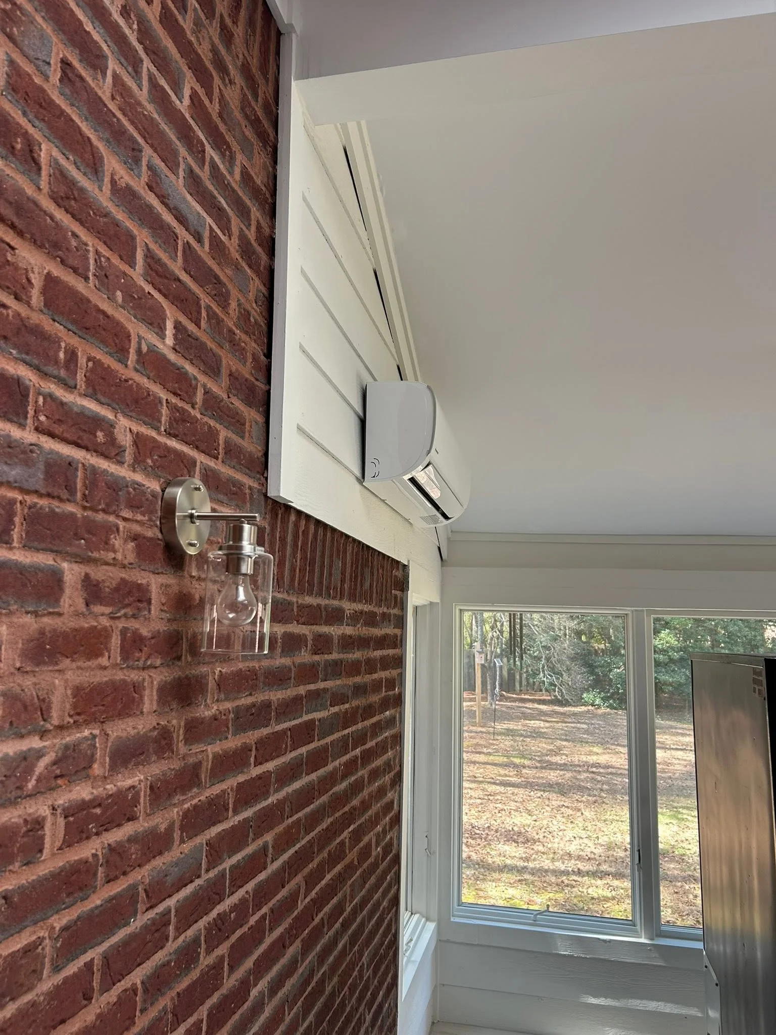 Ductless mini split indoor unit mounted on white ceiling soffit beside exposed brick wall