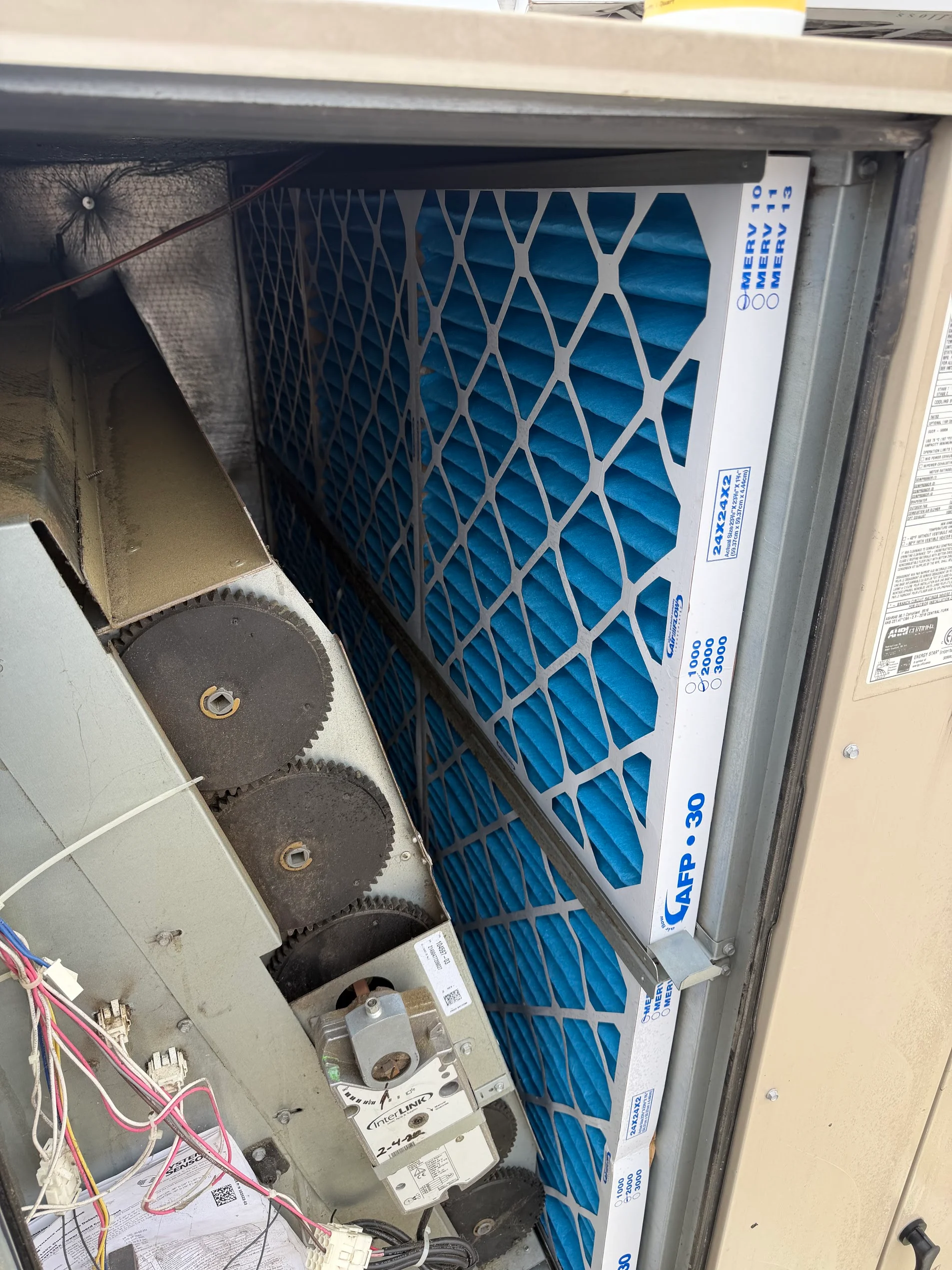 New pleated air filter installed in HVAC unit with blower wheels and internal components visible