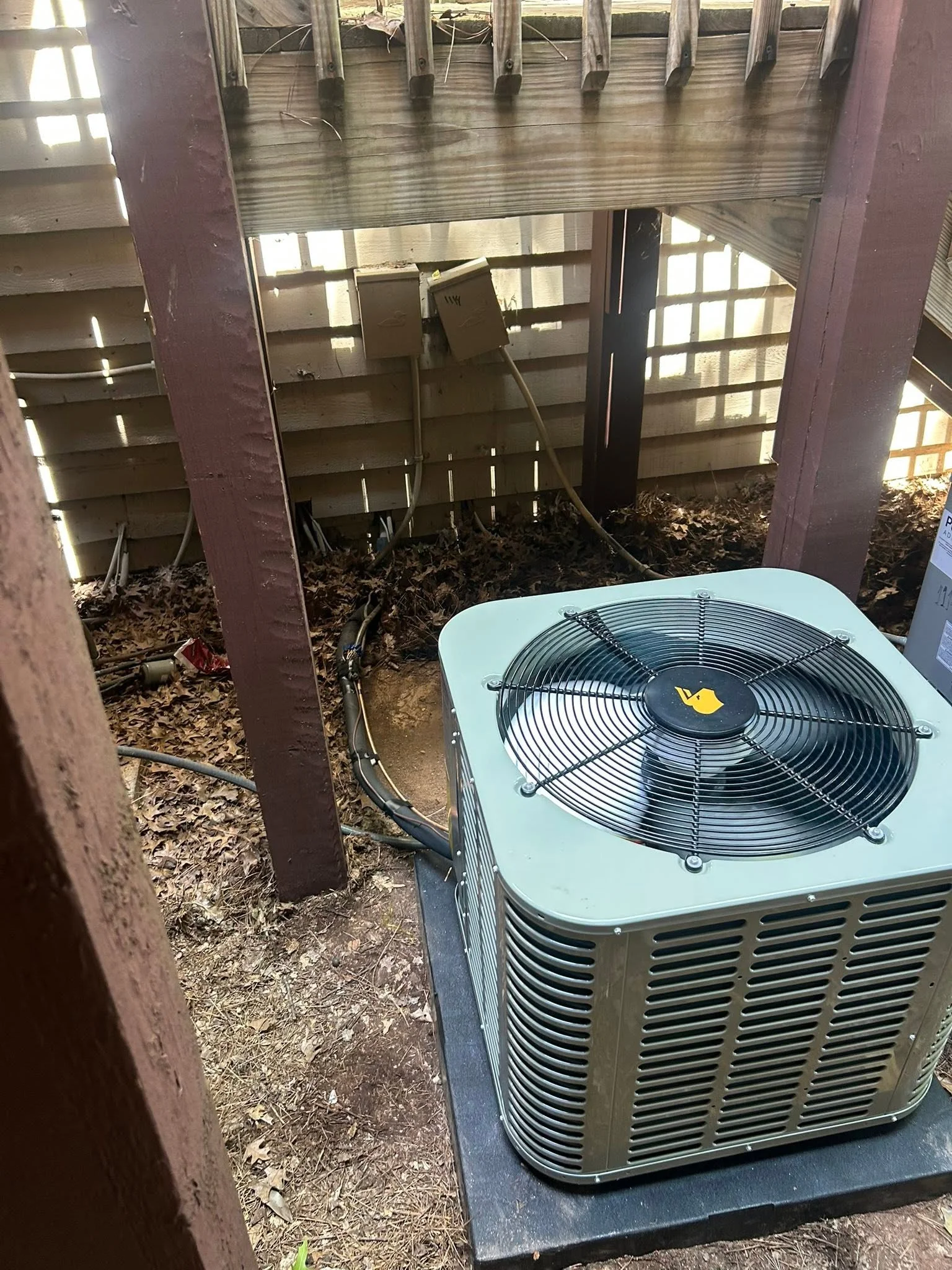 New AC condenser unit with fan on concrete pad, refrigerant lines routed through support posts