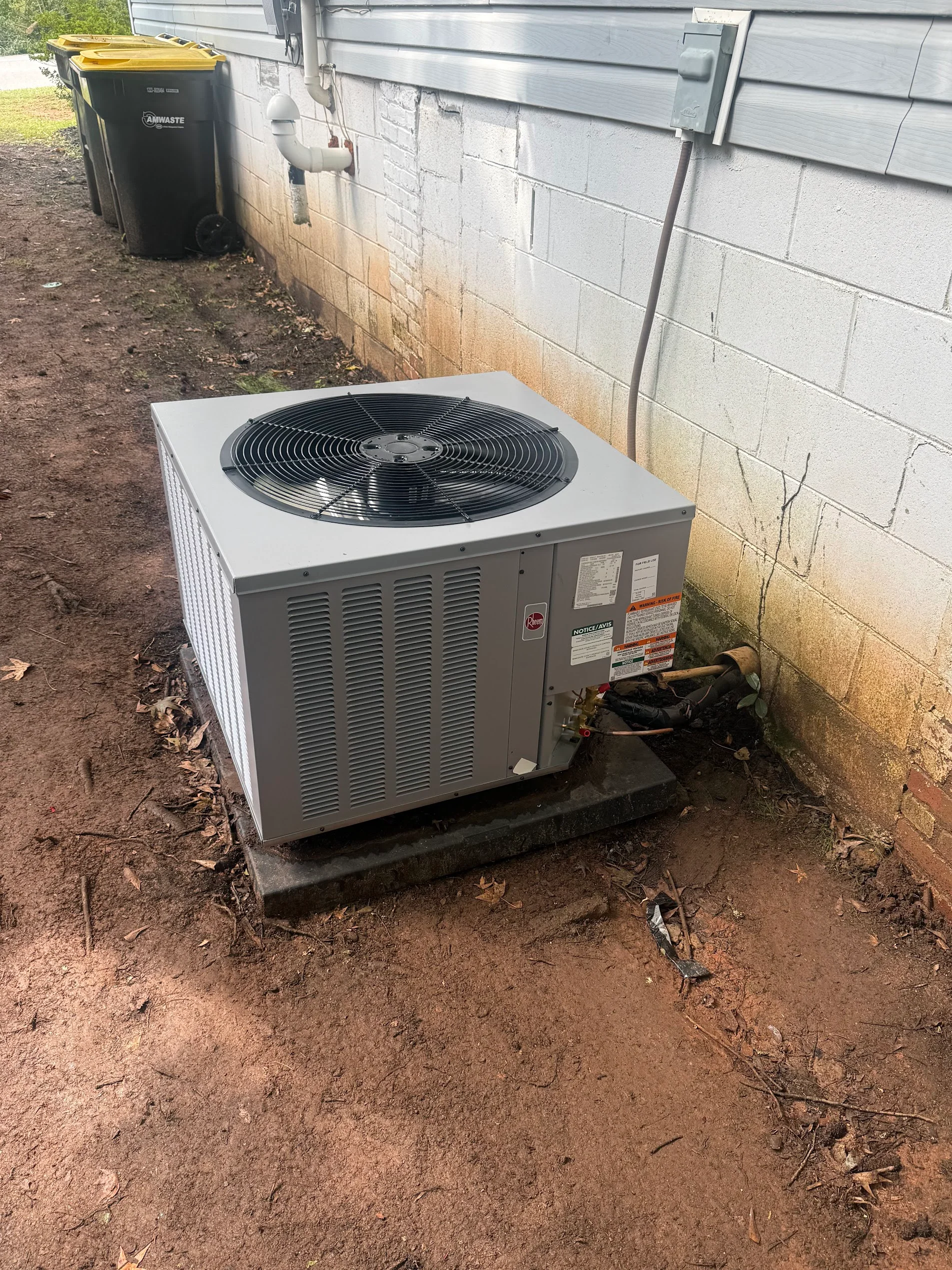 Gray packaged AC unit with black fan motor on concrete pad, refrigerant lines and electrical connections installed