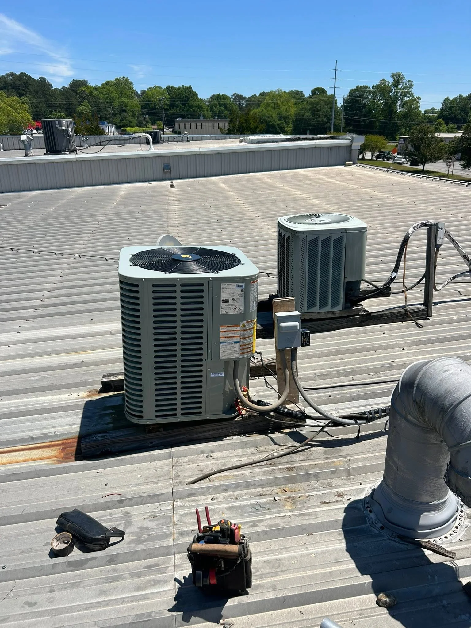 Two rooftop AC units with refrigerant lines and ductwork on commercial metal roof installation