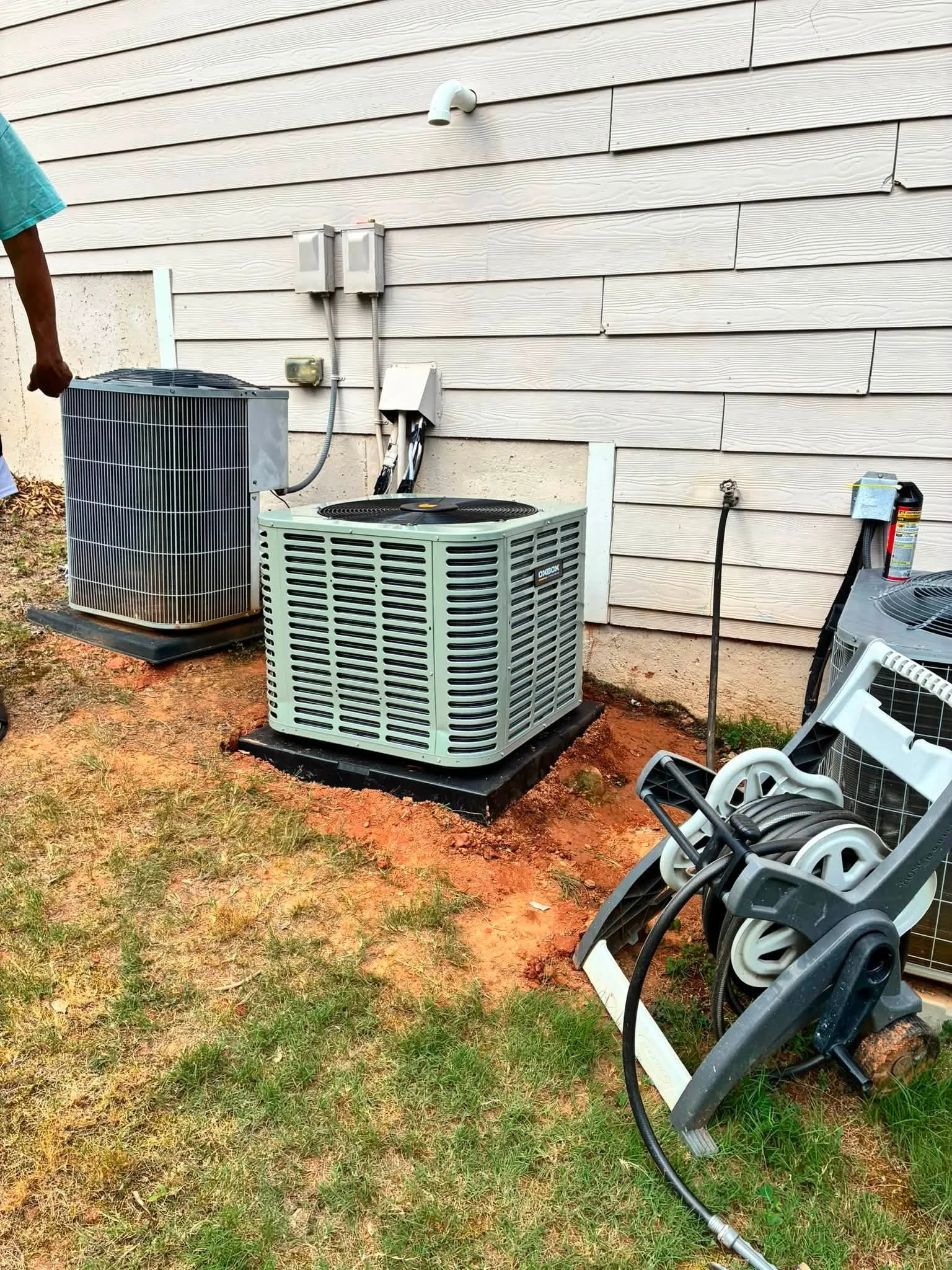 New AC condenser unit installed on ground pad with electrical connections and refrigerant lines
