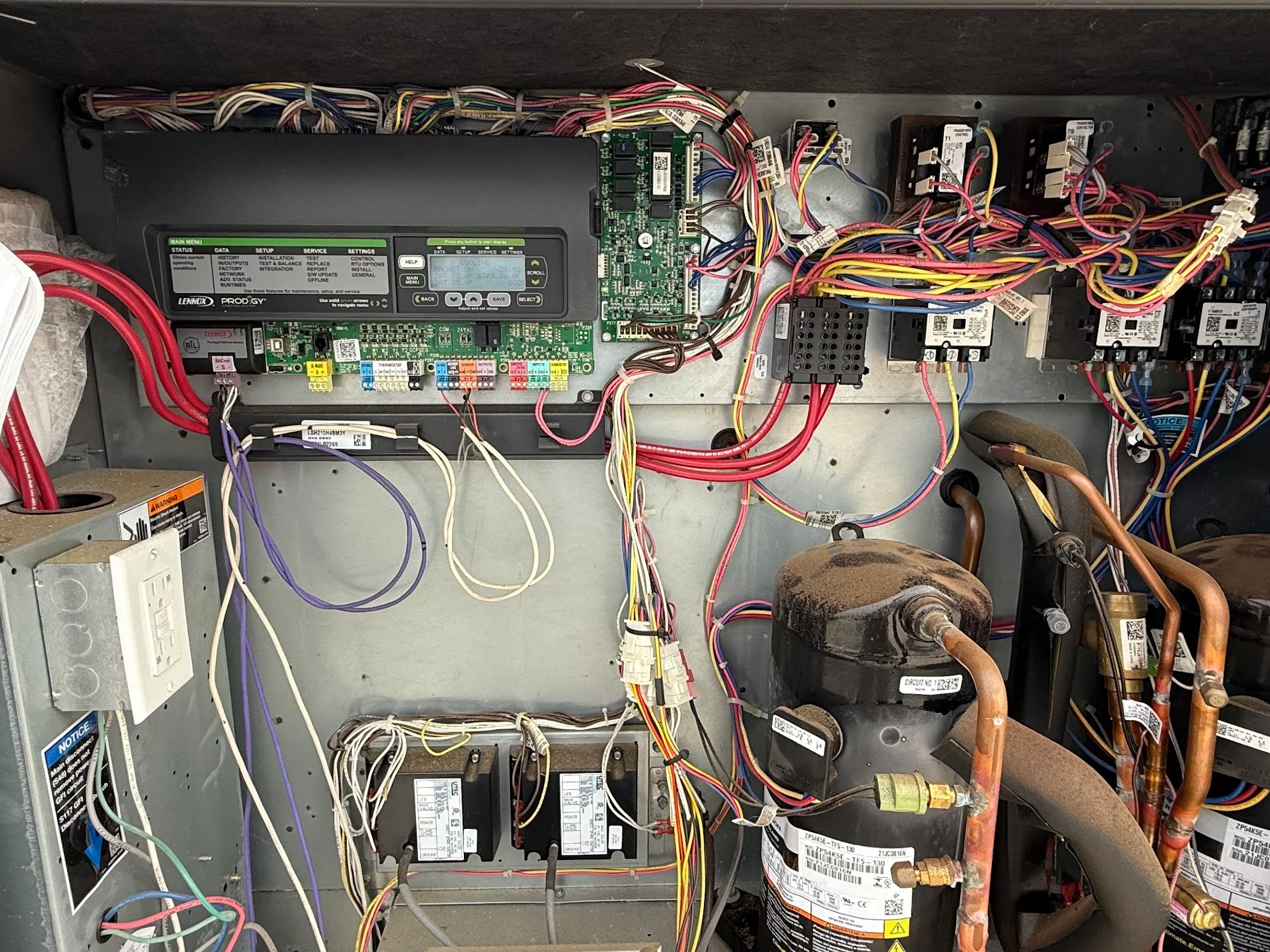 HVAC control board with circuit modules, colored wiring, compressors, and refrigerant lines in metal enclosure