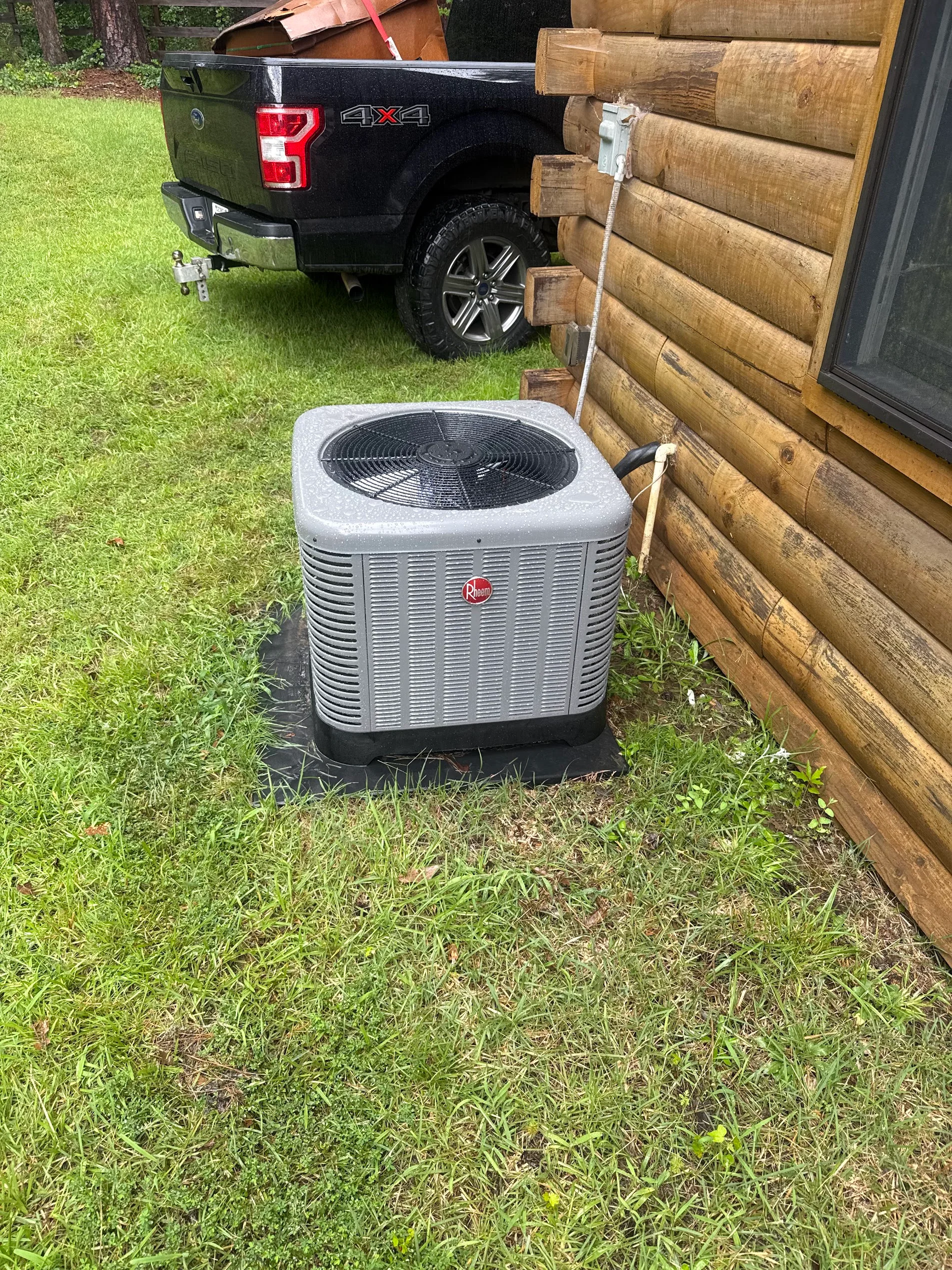 Rheem heat pump condenser unit installed at log cabin with refrigerant lines and electrical connections
