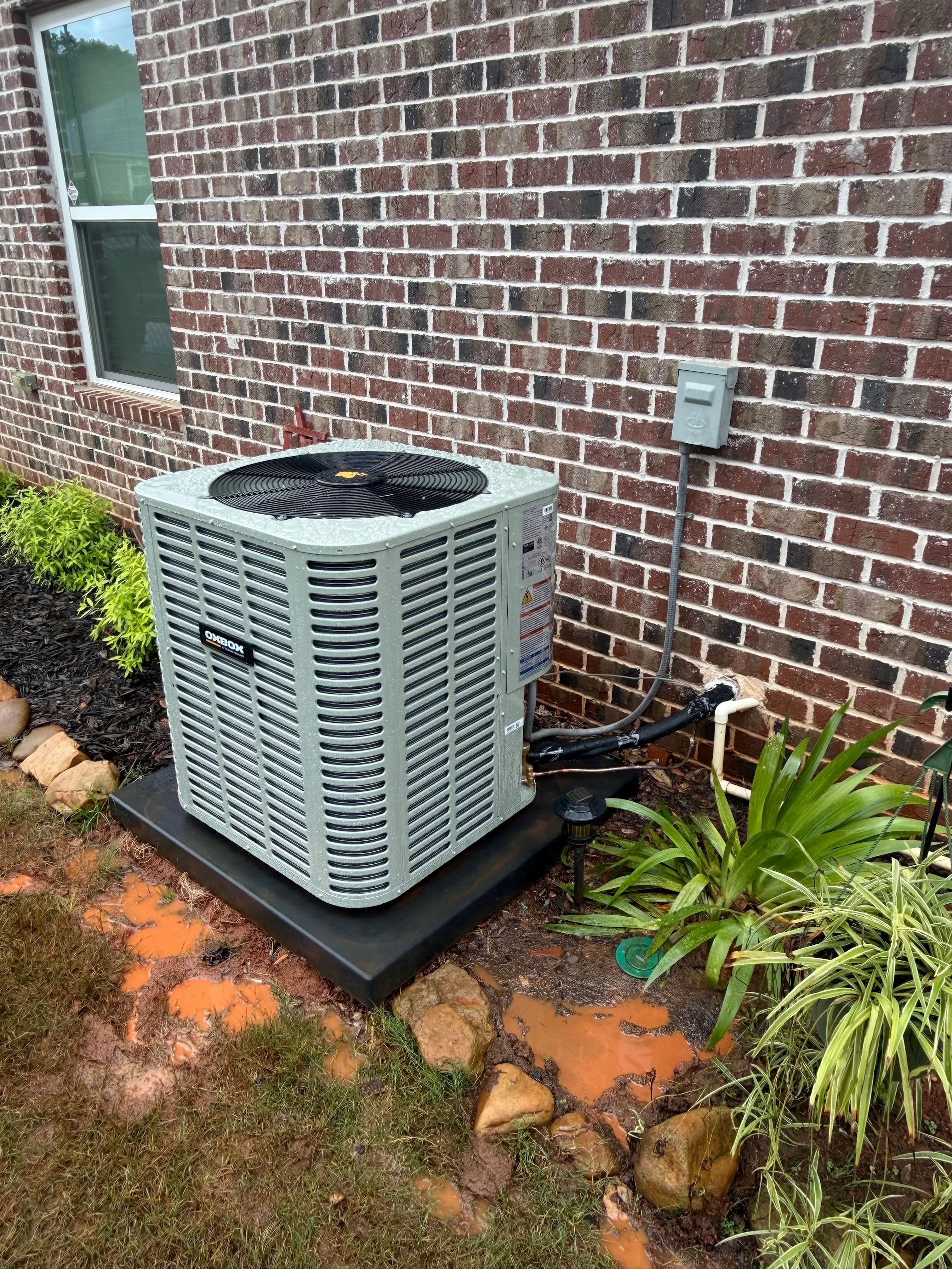 New air conditioning condenser unit on concrete pad against brick wall with electrical connections