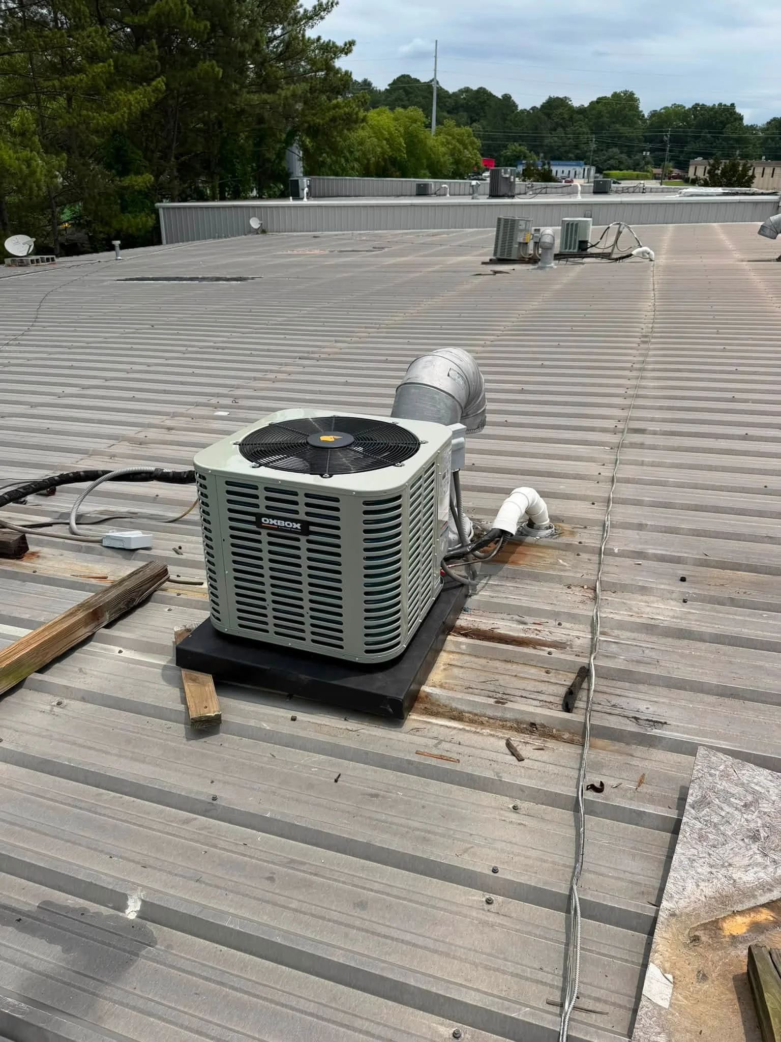New AC condenser unit installed on commercial metal roof with electrical connections and mounting base