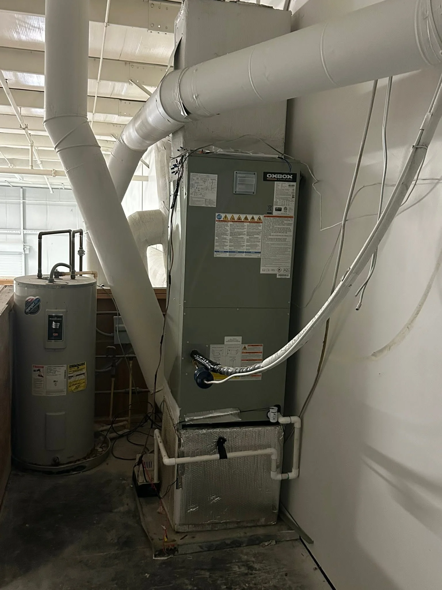 HVAC air handler unit with insulated ductwork, water heater, and metal flex connectors installed in utility space