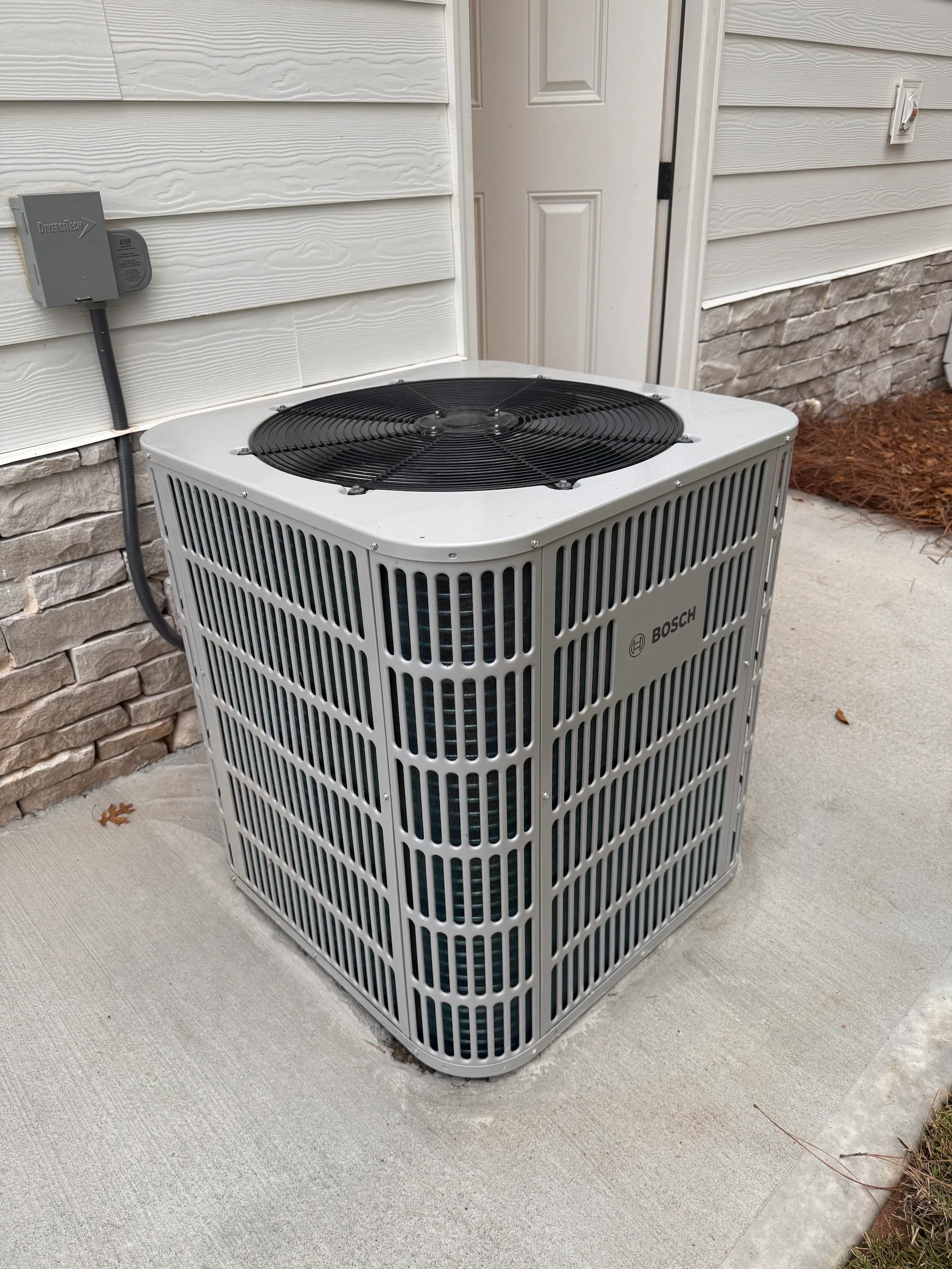 Bosch air conditioning condenser unit with black fan motor on concrete pad