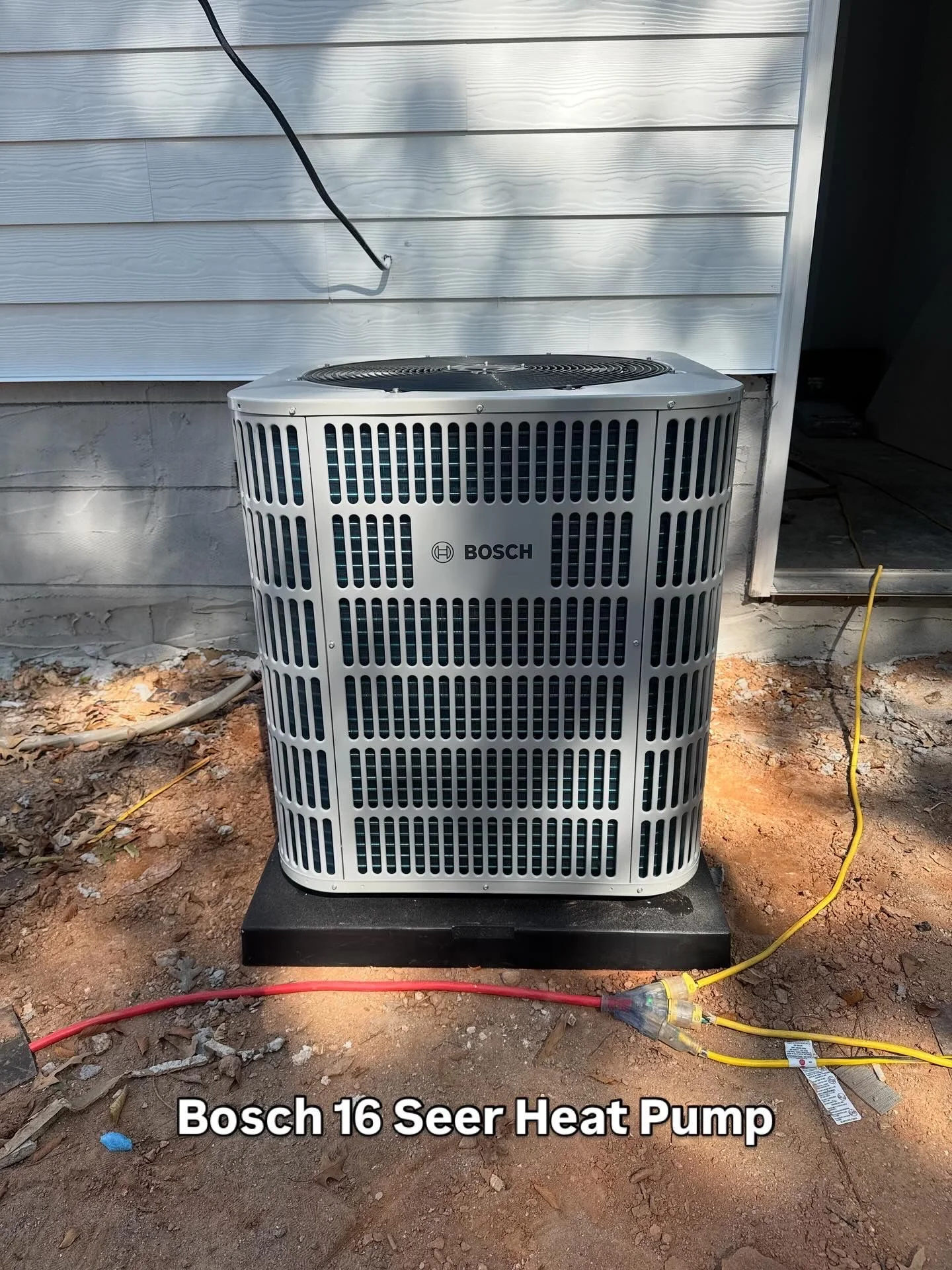 A Legacy HVAC Services technician completing a heat pump installation at a single-family home in Hampton, GA, with the outdoor condenser unit mounted on a pad beside the house. The home reflects the detached residential style common across Henry County neighborhoods.